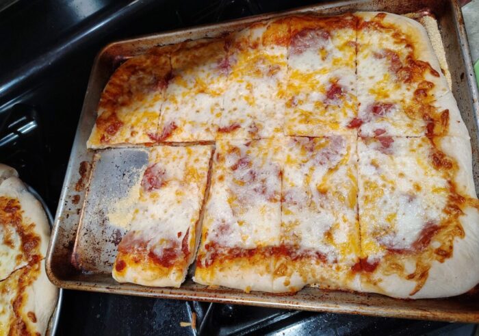 A sheet pan of pizza with a reglar, round pizza hiding in the corner of the picture