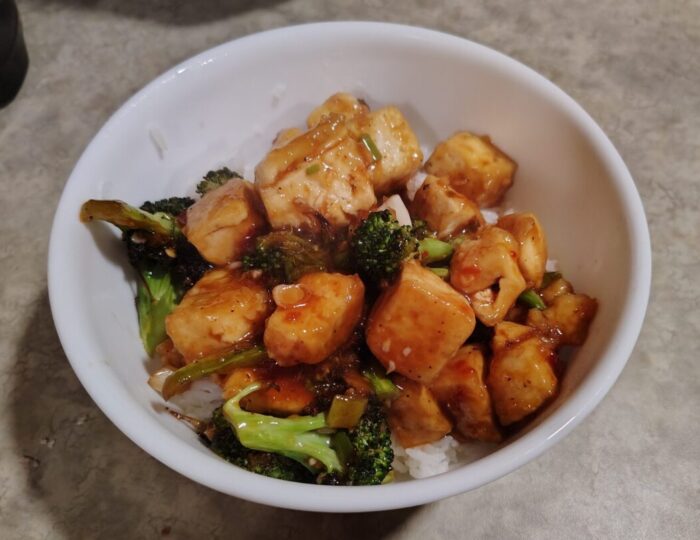 A bowl of rice topped with tofu and broccoli in orange sauce