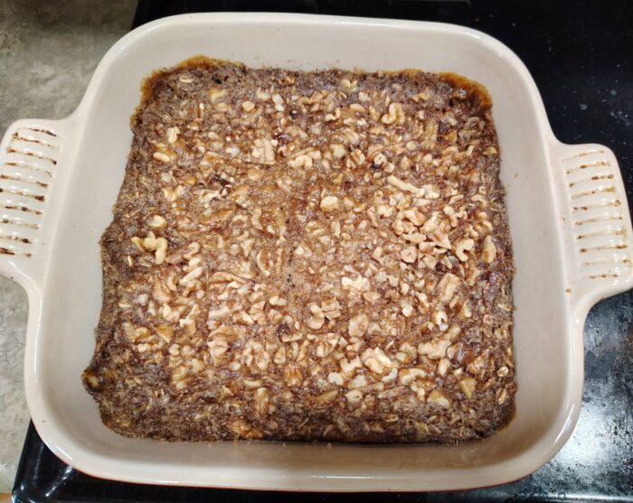 A square ceramic pan of baked oatmeal topped with walnuts