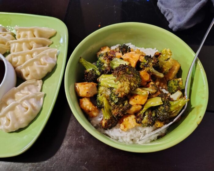 A bowl of orange tofu and broccoli over rice next to a plate of gyoza