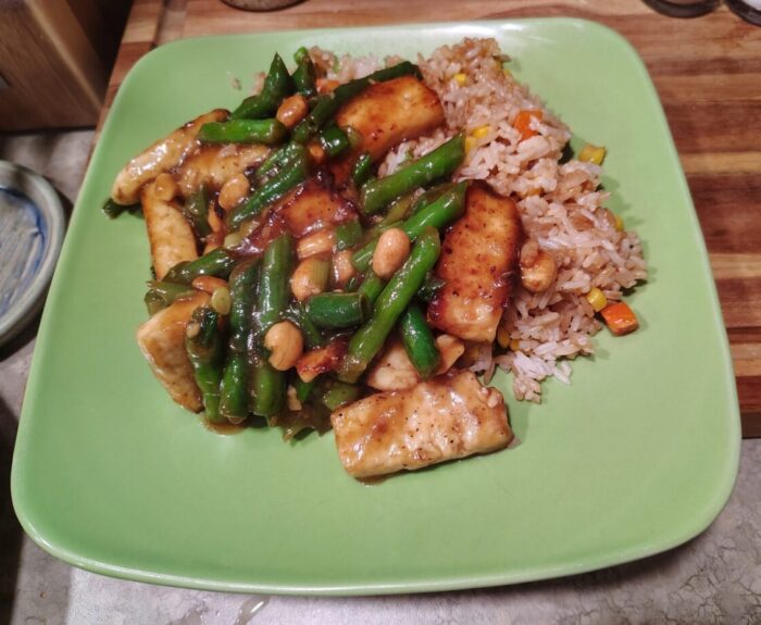 A plate of tofu, green beans, and peanuts coated in a thick glaze over fried rice