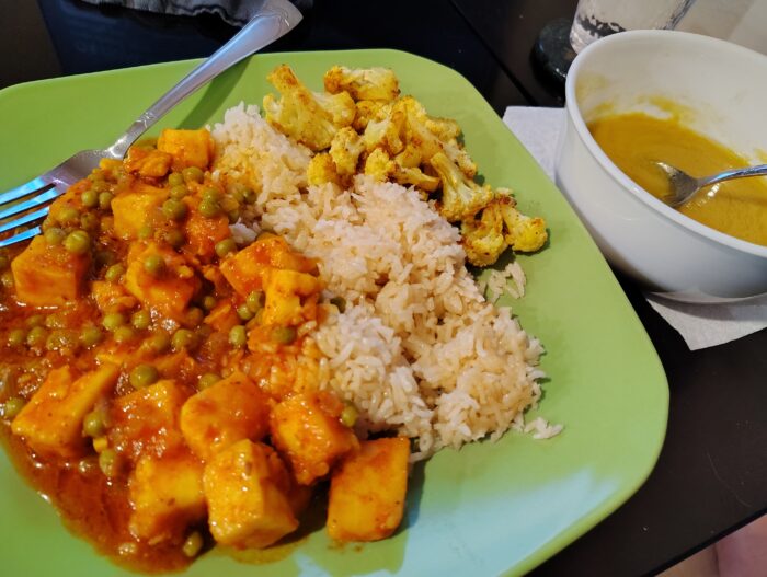 a plate of matar paneer, rice, and roasted cauliflower and a bowl of garlic dal