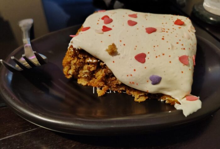 A cookie bar with white marshmallow creme frosting draped over it and topped with heart sprinkles