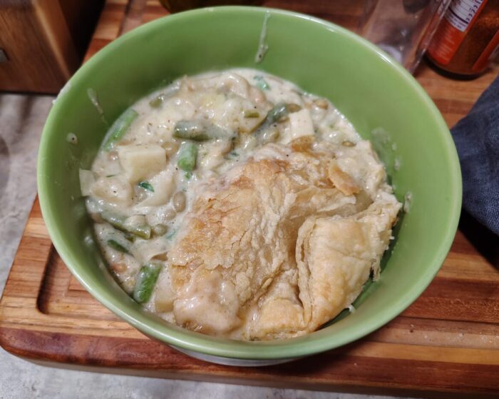 a bowl of soupy pot pie with potato, beans, and green beans topped with puff pastry