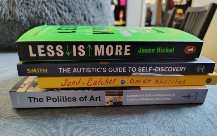 a small stack of books including: Less is More, The Autistic's Guide to Self-Discovery, Sand-Catcher, and The Politics of Art