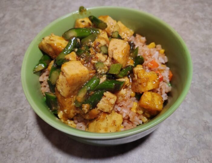 A bowl of fried rice topped with stir-fried tofu and asparagus