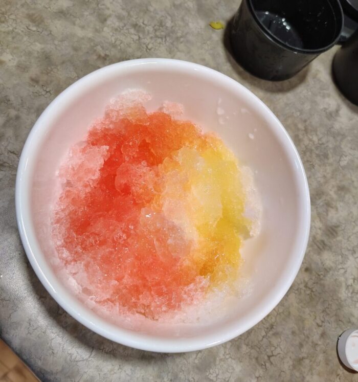 a bowl of shaved ice topped in red and yellow syrups