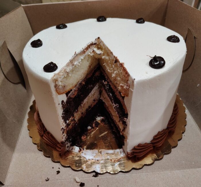 a cake with a big slice removed revealing alternating white and chocolate layers. The cake is covered in white icing with chocolate accents