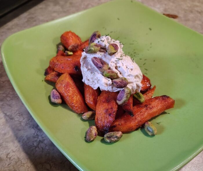 a pile of roasted carrot chunks topped with whipped tahini, pistachios, and a sprinkling of dill