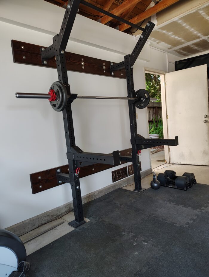 Squat rack with a bar (115 pounds total) in my garage gym. Side door is open to reveal trees
