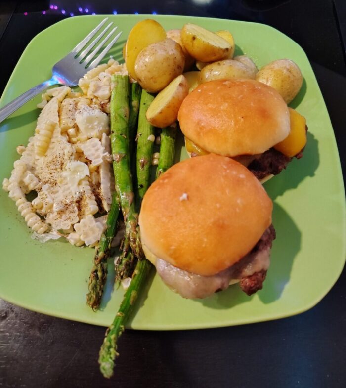 a plate of corn off the cob, asparagus, roasted potatoes, and two small cheeseburgers