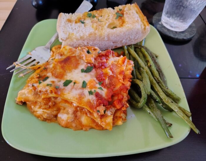 A plate with a big piece of lasagna, garlic bread, and roasted green beans