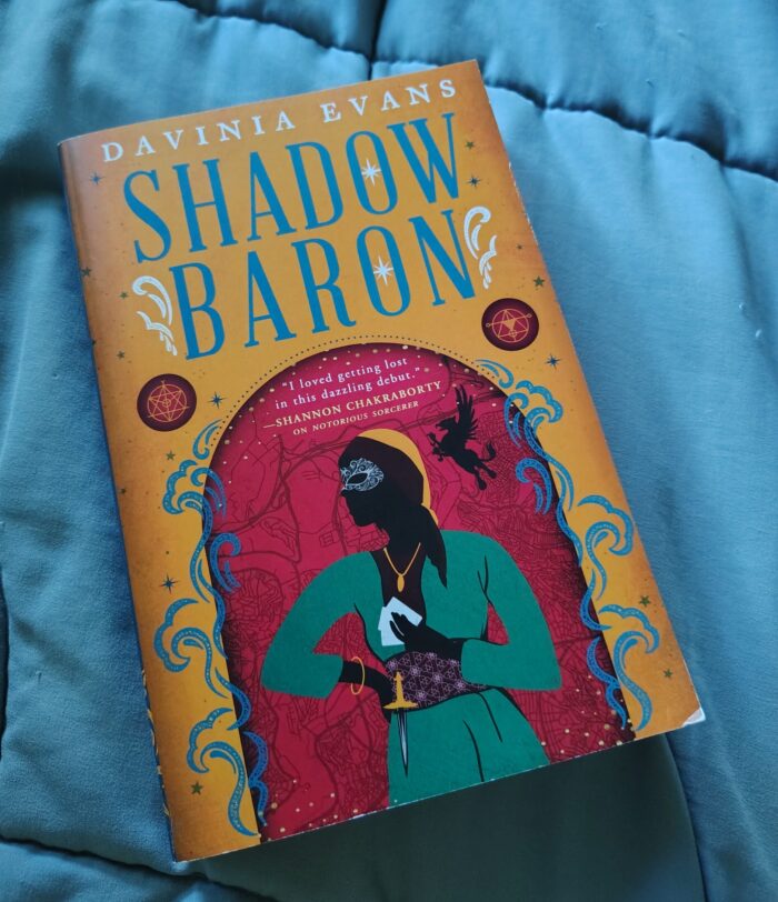 Paperback book: Shadow Baron by Davinia Evans. The cover is colorful and has a silhouette of on of the characters