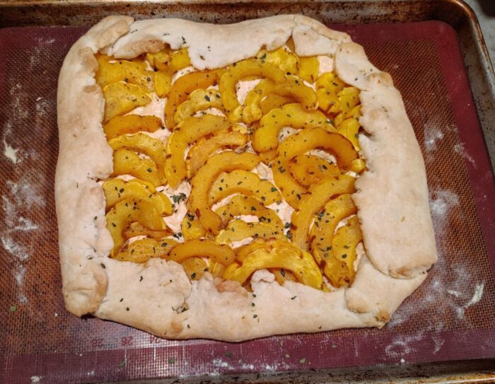 a pastry covered in cheese then topped with slices of delicata squash and herbs