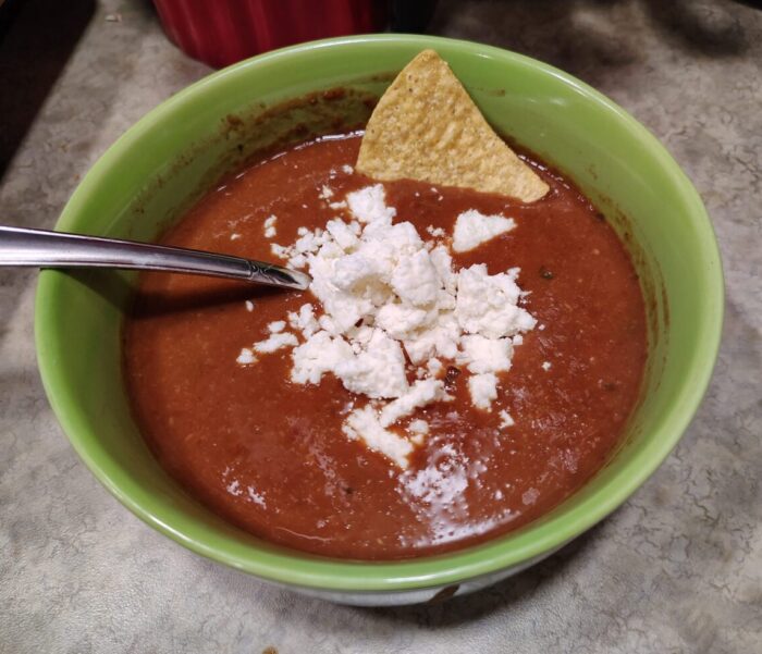 a bowl of blended bean soup topped with a pile of crumbled cheese and with a tortilla ship sticking out of it