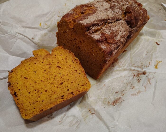a loaf of pumpkin bread with the top coated in cinnamon sugar. A slice is cut off to reveal its orange interior