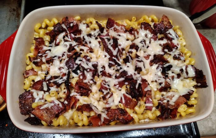 a casserole dish of baked macaroni and cheese topped with a generous amount of bacon and a little extra cheese melted over it