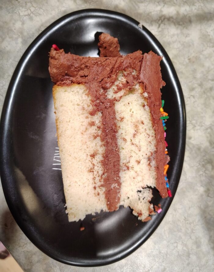 a slice of white cake with chocolate frosting being served on its side on a plate