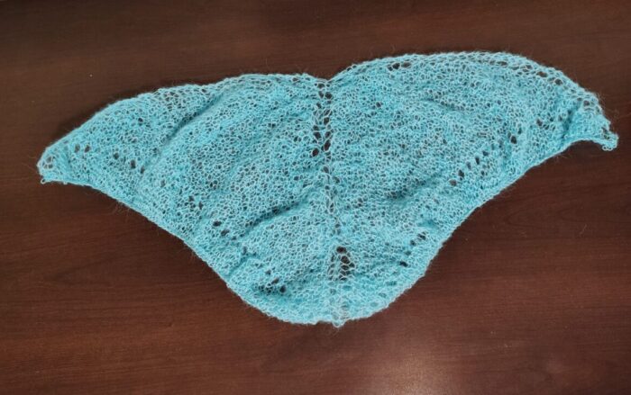 a small, triangular shawl in glacial blue. The yarn is very thin and the shawl is a lacey design