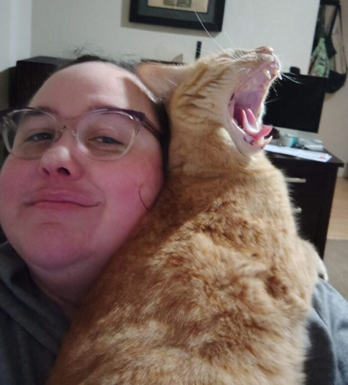 Me holding fritz the cat. He's leaning the back of his head and neck against my face and his mouth is all the way open to yawn