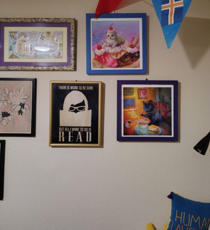 Art arranged on my wall including a new addition of a black cat eating a soup and a sandwich at a celestial witchy 90s themed cafe