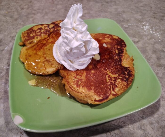 a plate of pumpkin pancakes topped with syrup and whipped cream