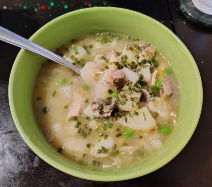 a bowl of soup featuring pieces of potato and turkey, topped with chives