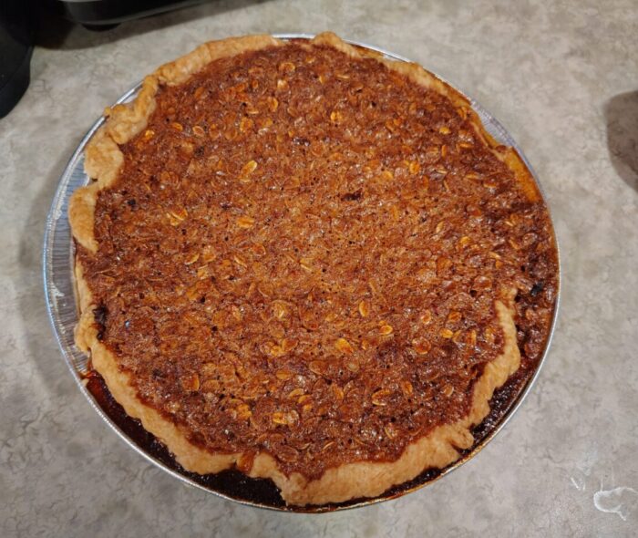 a pie still in the tin. The caramelly oat mixture is overflowing the crust a little