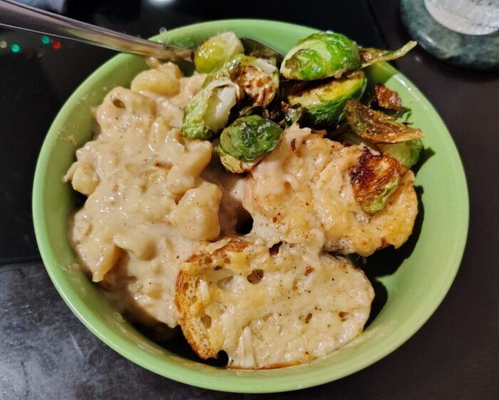 a bowl of thick macaroni and cheese topped with bits of cheesy toast, with some roasted brussels sprouts piled to the side