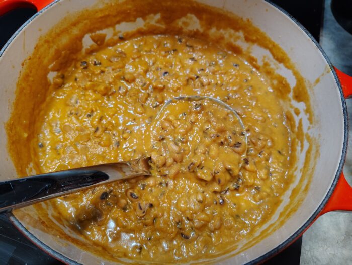 a pot of black-eyed peas in an orange-colored coconut and tomato sauce