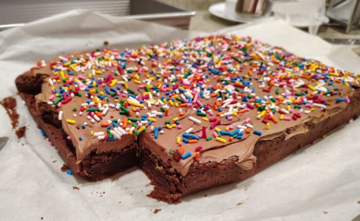 A batch of brownies topped with chocolate frosting and rainbow sprinkles