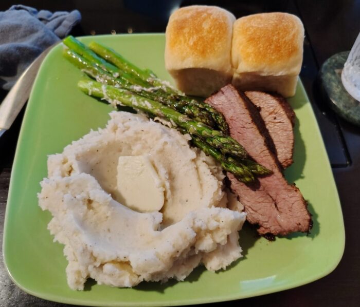 a plate of tri-tip, mashed potatoes, asparagus, and rolls