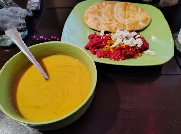 a bowl of red lentil soup, alongside beet cous cous topped with feta and a spiced nut mixture, and a naan