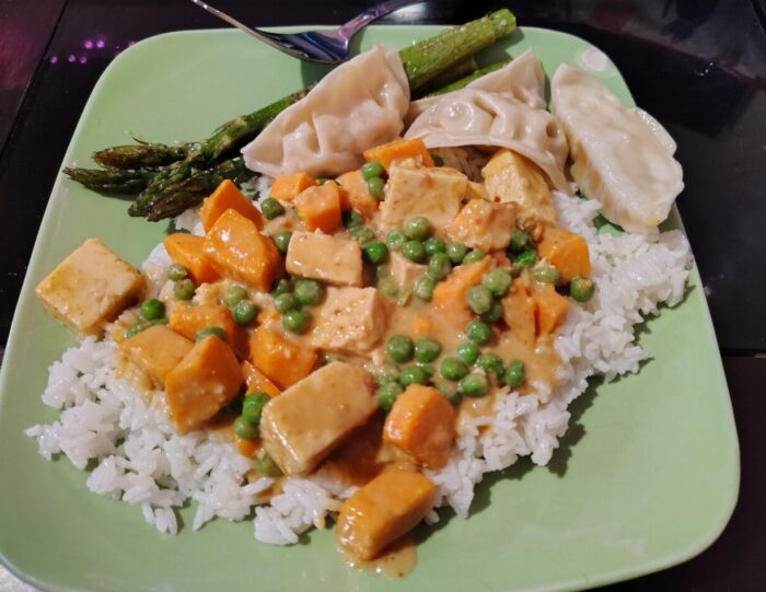 a plate of tofu and sweet potato curry over rice, a few spears of roasted asparagus, and some pot stickers