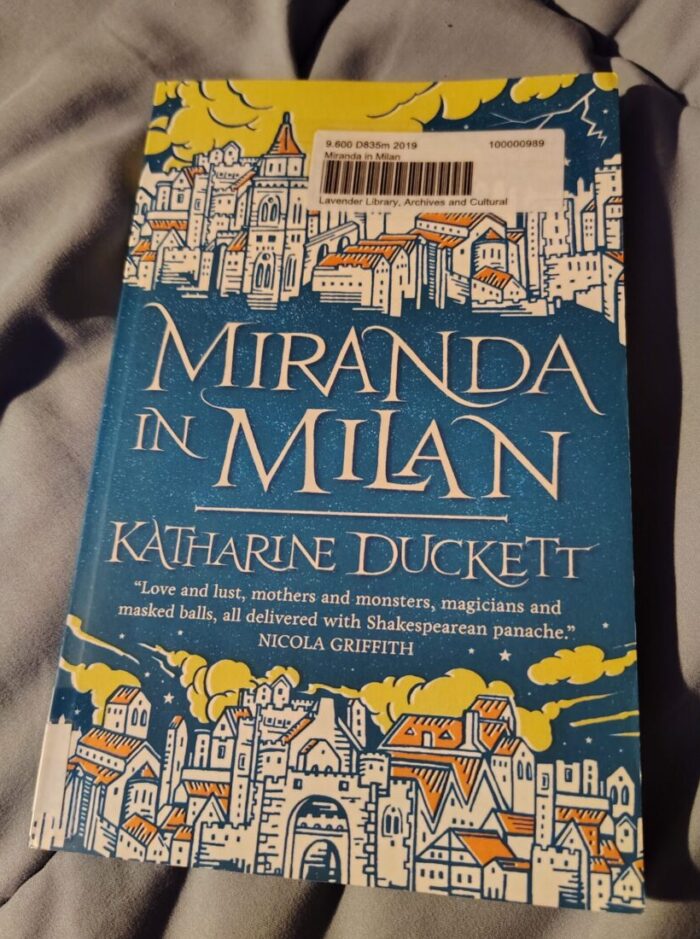 book cover of Miranda in Milan featuring a charmingly illustrated medieval cityscape