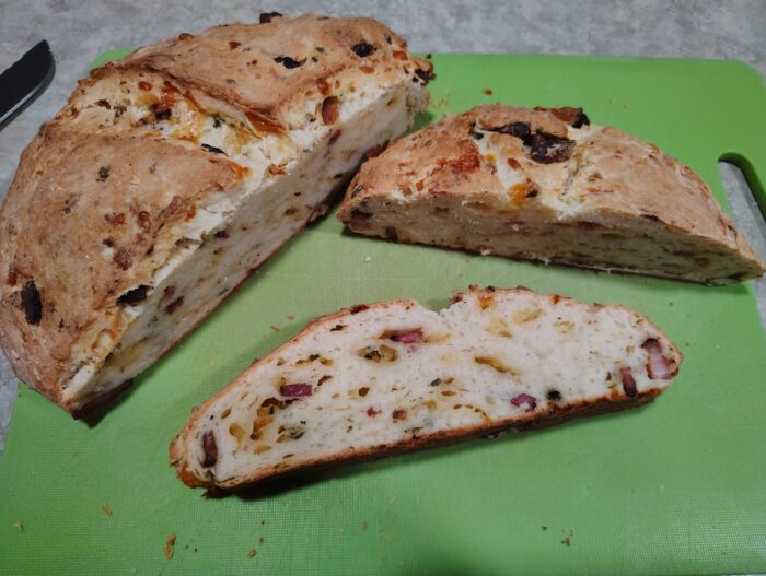 a squat loaf of bread not unlike a soda bread cut in half to show that it is studded with cheese, bacon, and chives