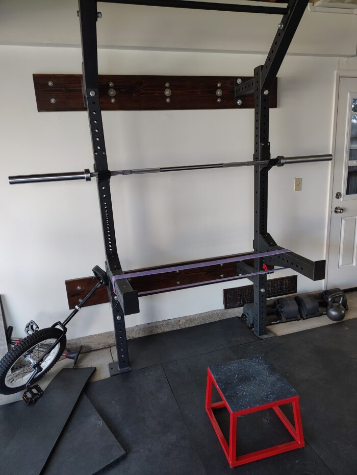 squat rack with a thick elastic band positioned for bar hang support, a 12-inch platform in front of it to step up onto the band