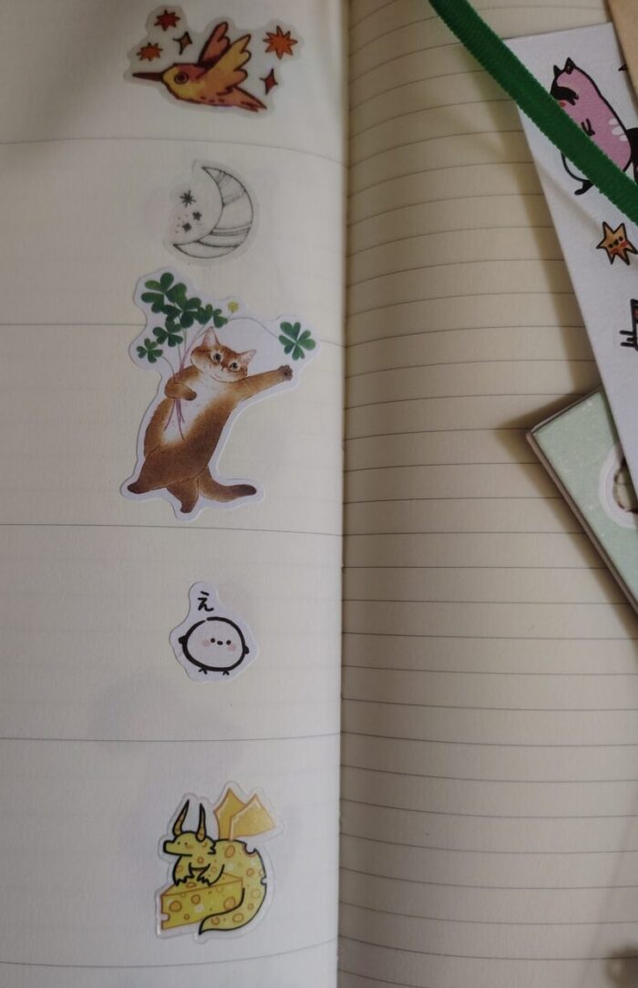 stickers in my planner including a sparkly bird in flight, a crescent moon, an orange cat with flowers, a fat bird, and a cheese dragon