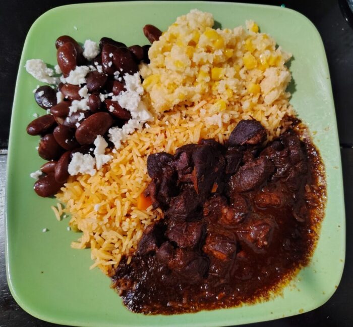 a plate of chili colorado, rice, beans, and corn cake