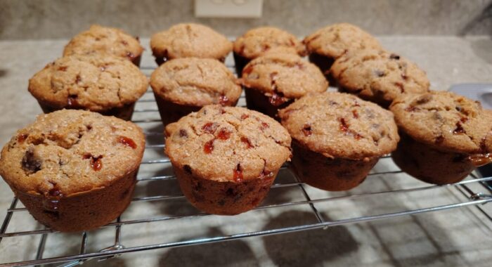 a dozen muffins cooling on a wire rack. Jammy bits are oozing out