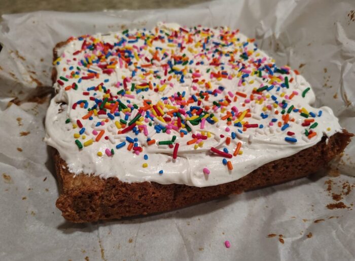 a square oatmeal cake topped with fluffy marshmallow frosting and a bunch of rainbow sprinkles