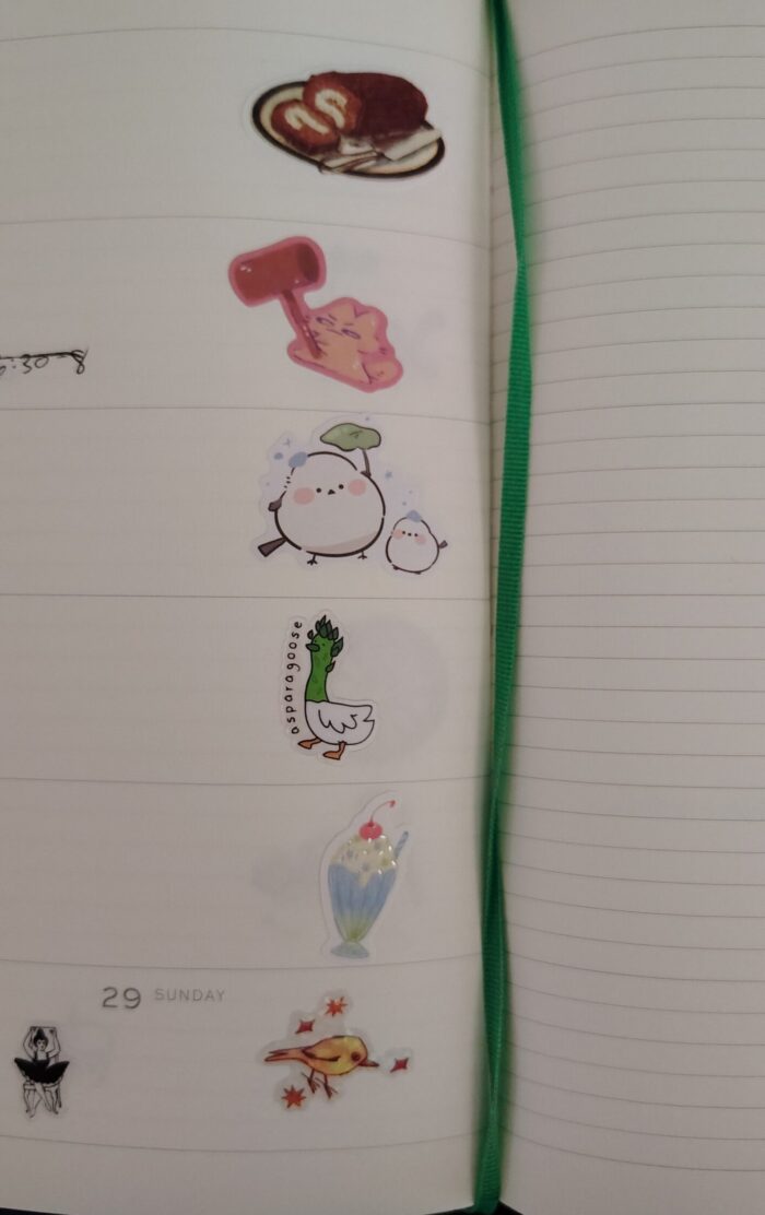 stickers in my planner including a swiss roll cake, a mischievous bunny with a mallet, a cute bird, a goose with an asparagus neck, a milkshake, and a ballerina