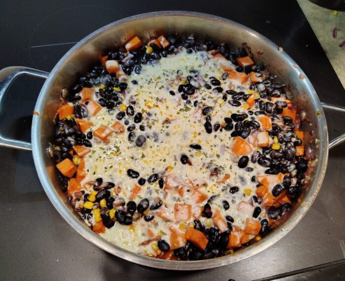 a skillet of black beans, corn, and sweet potato covered in melted cheese