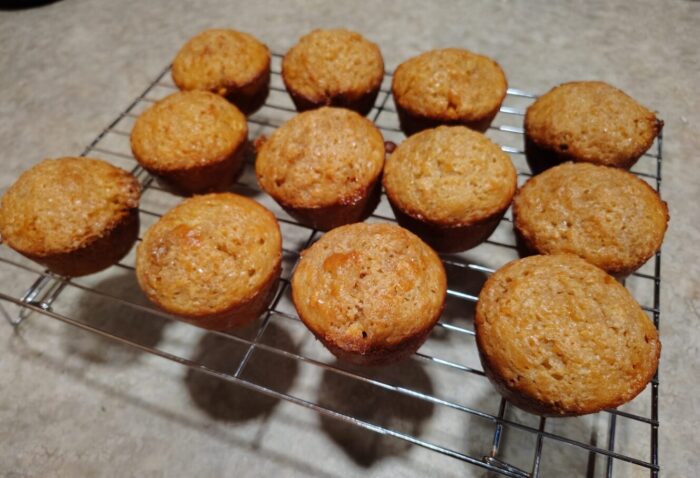 a dozen muffins cooling on a rack. They have oats and butterscotch chips inside and are topped with turbinado sugar