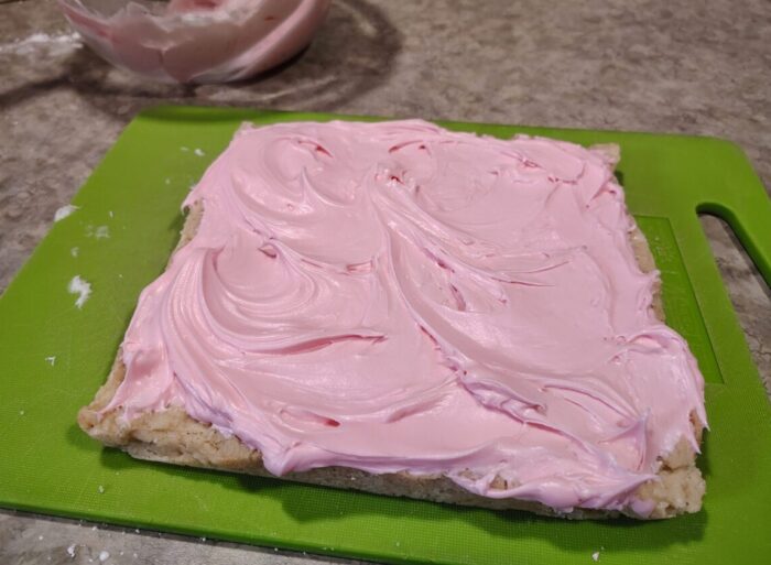 a square shortbread cookie topped with a thick swirl of pink cream cheese icing