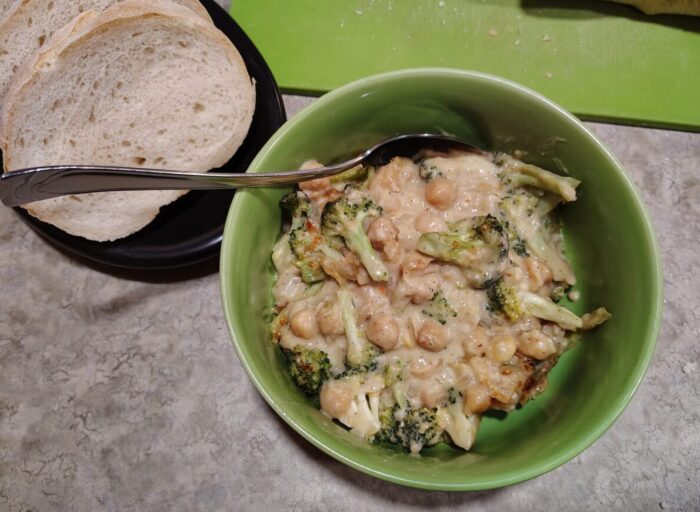 a bowl of chickpeas and broccoli cooked in a creamy sauce, with some bread on the side