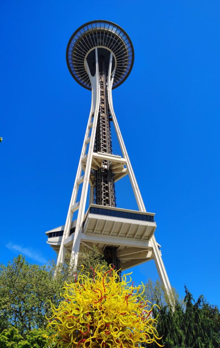 View of the space needle behind one of a wiggly yellow glass sculpture in the Chihuly garden and glass exhibit on a perfectly clear day