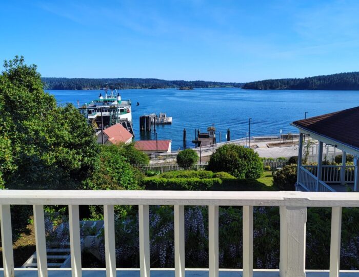 stunning view of the Salish sea and Shaw Island, along with the ferry docked, from the Orcas hotel. It's a clear day and the sea is bright blue.