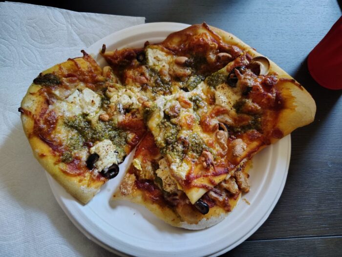 a paper plate with a large-ish personal pizza topped with a smattering of pepperoni, cashews, olives, beans and some pesto and goat cheese