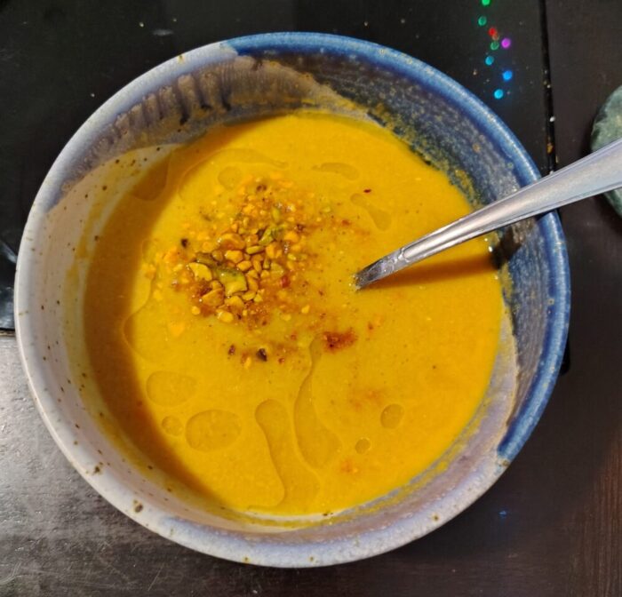 a bowl of red lentil soup topped with spiced, chopped nuts and a drizzle of olive oil